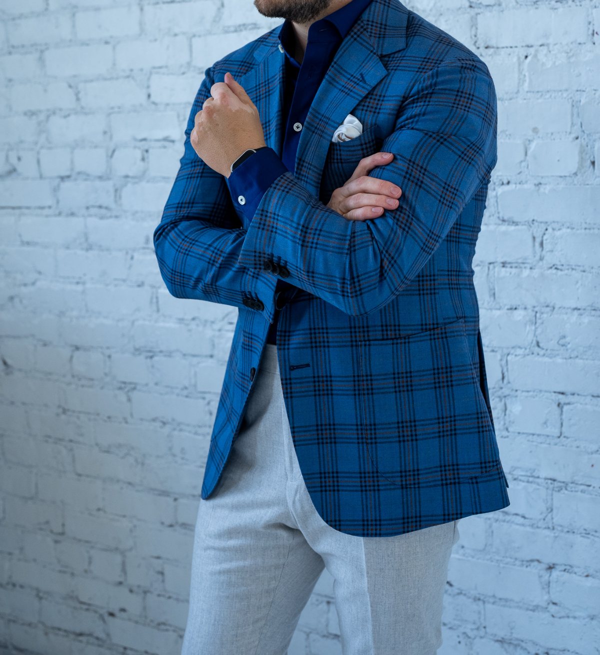 A Smith Bespoke blue check sport coat, worn against a white brick wall